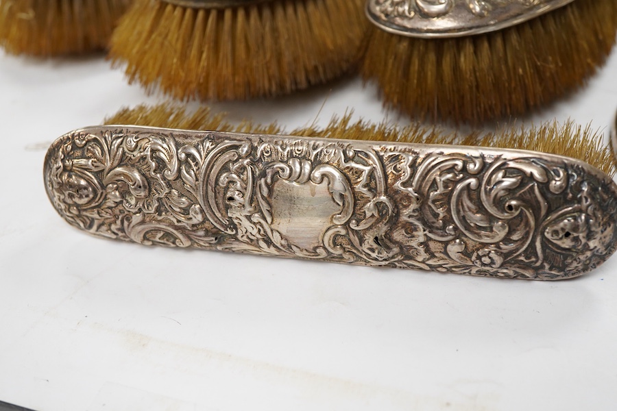 A late Victorian embossed silver four piece dressing table mirror and brush set, by William Comyns, London, 1891/5 and a similar clothes brush.